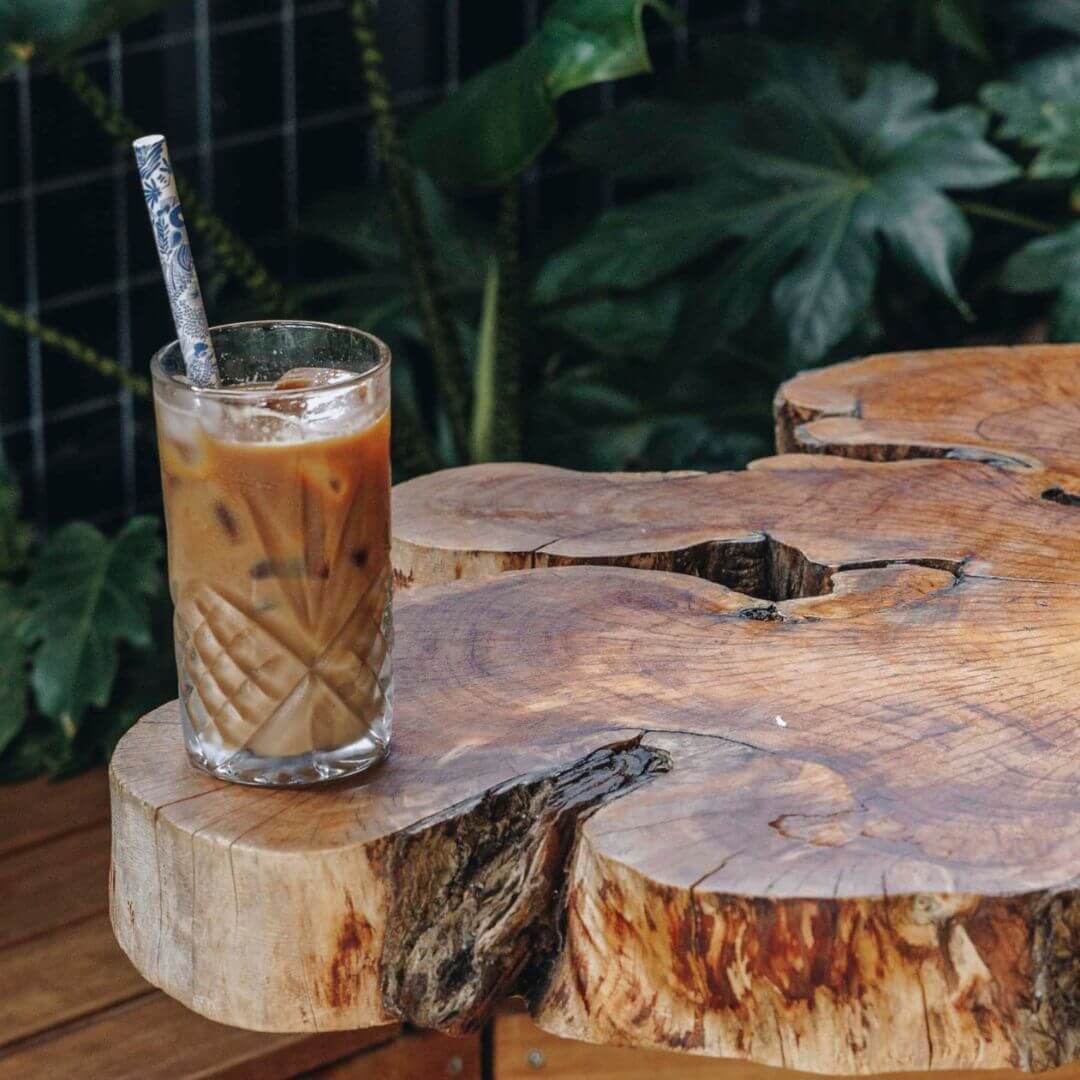 A large iced latte in a glass sitting on a table made from a wooden tree slice.